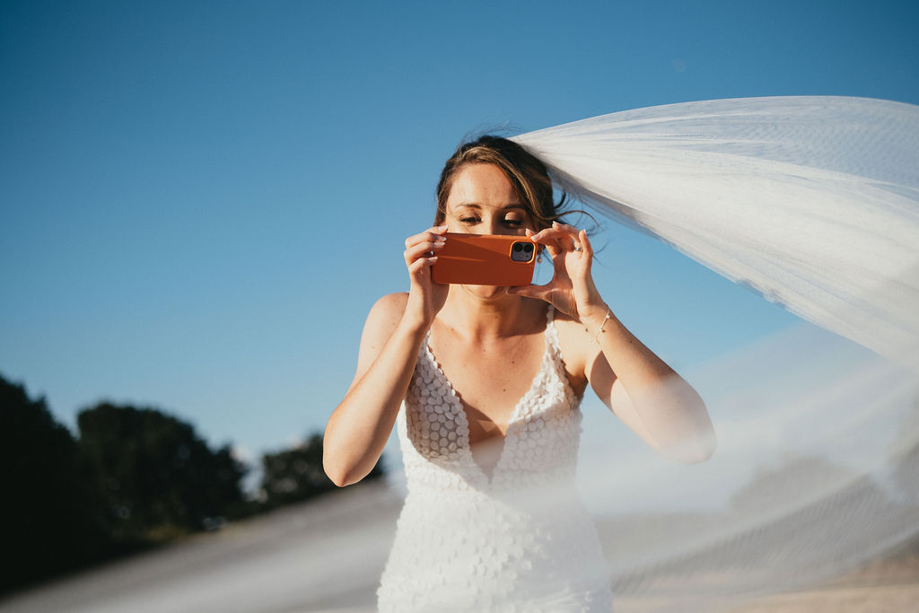 Bride take a phone on her iphone with her veil blowing on the wind