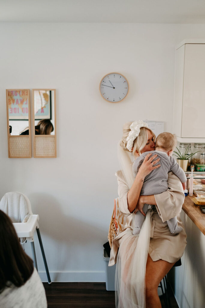 Bride in a dressing gown holding her baby in the kitchen