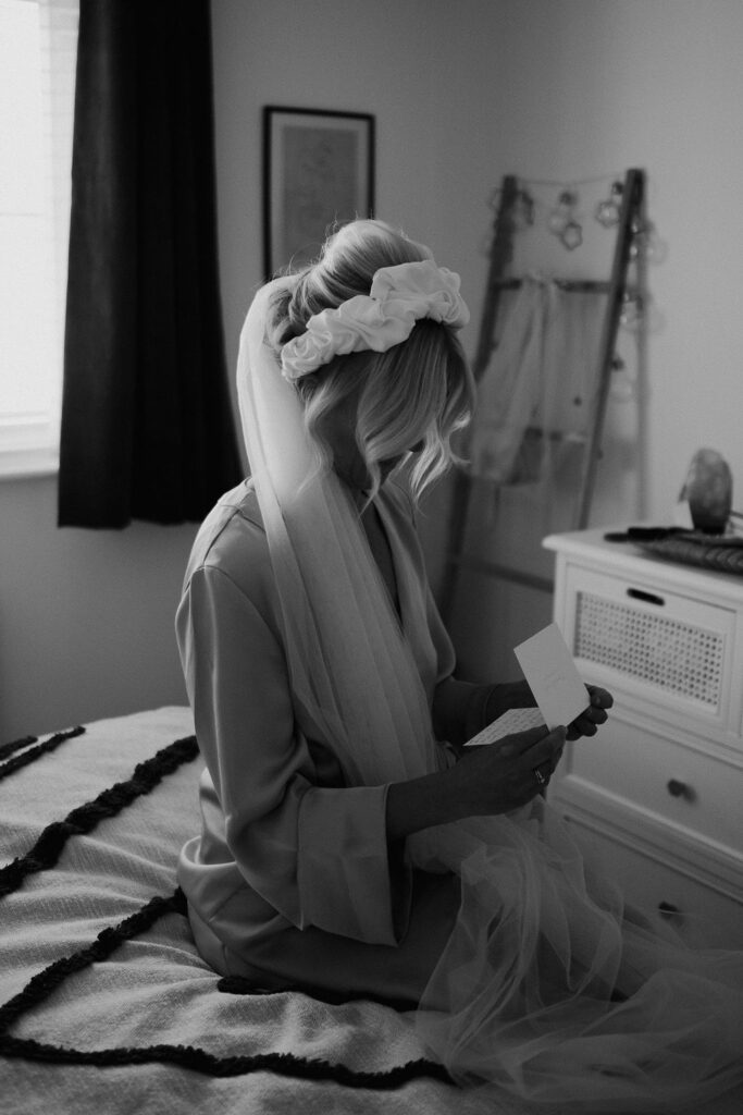 Bride reads a love note on her bed wearing a veil and dressing gown