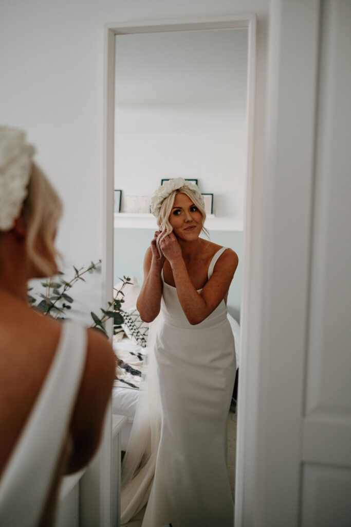 bride looking in the mirror putting her earrings in