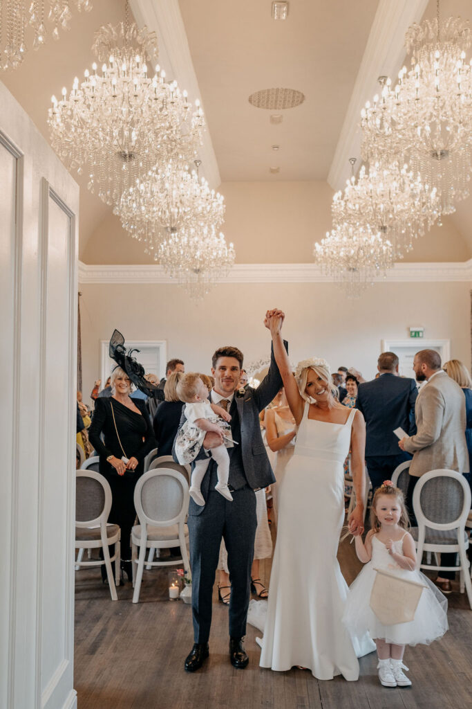 bride groom and their daughters walk down the aisle with their hands in the air.