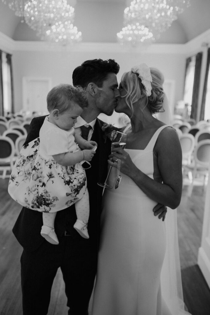 couple kiss whillst holding their young daughter at Amalfi White Wedding