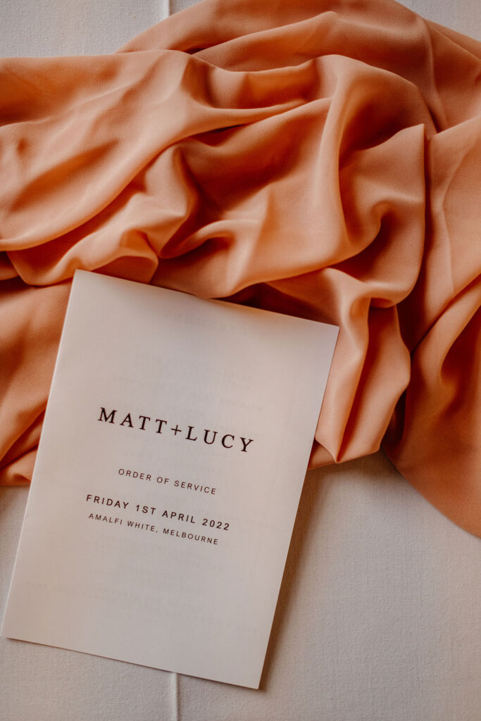 modern order of service on pink silk backdrop at an Amalfi White Wedding