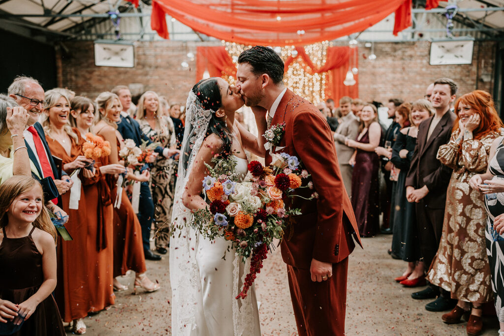 Confetti with a lace veil and a groom in a red suit. 